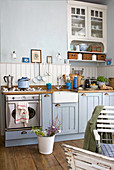 Landhaus Küchenzeile in hellblau und weiss gestrichenem Holz mit modernem Edelstahlherd und Gartenstühlen am Sitzplatz