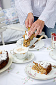 Romantischer Kaffeetisch mit altem Porzellan; Frauenhände legen Kuchenstück auf einen Teller