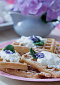 Waffles with cream and candied flowers on a pink plate