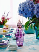 Violette Gläser zwischen Gedecken und Hortensienblumen auf Tisch