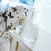 A glass carafe filled with water and glass on a side table
