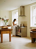 Frau schmeckt Essen ab in schlichter Küche mit rustikalem Tisch und Designer Küchenofen