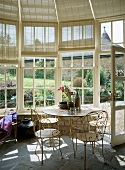 Delicate, white-painted metal table and chairs in vintage glass pavilion
