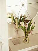 Bouquet of white tulips and candlestick on white shelf below mirror