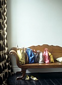 Baroque, wooden bench with collection of colourful bags on dark wooden floorboards