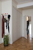 Glass vase below coat rack and white fitted wardrobes in foyer