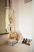 High-heeled shoes next to stack of books and embroidered top on coat hanger in corner of room