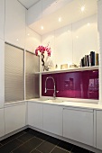 Kitchen counter with white doors and purple glass backsplash in designer kitchen