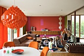 Red, retro pendant lamp above dining area and children on sofa in open-plan living space