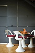 Dining area with white shell chairs and red cushions in front of wall clad in slate slabs