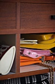 Colourful plastic handbags in open pigeonhole of shelves with mahogany veneer