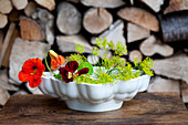 Nasturtium and dill flowers in old jelly mould on table in front of stacked firewood