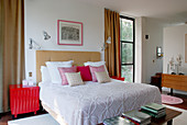 Doppelbett mit drapierten Kissen zwischen raumhohen Fenstern mit bodenlangen Vorhängen in klassisch modernem Schlafzimmer