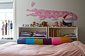 A crocodile and a heart cut out of patterned wall paper above a bed with a colourful relax pillow in a girl's bedroom