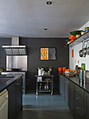 Graue Küchenzeile und Mittelblock vor Edelstahl Herd mit Dunstabzug an grau getönter Wand
