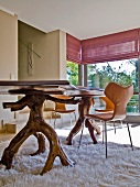 Dining table with legs made from unfinished, twisted wood on flokati rug in modern interior