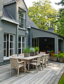 Long wooden table and chairs on terrace of house with grey brick walls