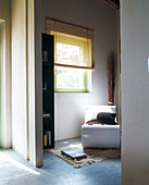 Moderner, weisser Lesesessel in blaugetöntem Raum mit grünem Fensterrahmen und herabgelassenem Sonnenschutz