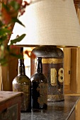 Two old bottles used for decoration next to a table lamp with the base made from an antique metal container