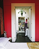 View from red-painted bedroom through open double doors into modern, white bathroom
