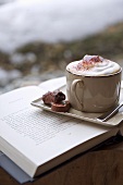 A cappuccino with pralines on a saucer sitting on a open book