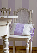 Old French chairs around wooden table in Gustavian style in front of purple and white striped wall
