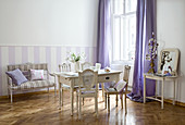 Old French chairs around wooden table in Gustavian style and bench against purple and white striped wall