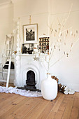 Decorated twigs in large, white vase on wooden floor next to open fireplace in traditional setting