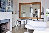 Moderner Loungebereich vor offenem Kamin und grosser Wandspiegel mit Holzrahmen in Wohnzimmerecke