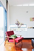 Sessel im 50er Jahre Stil vor weißem Sideboard und Fensterfront in Wohnzimmerecke