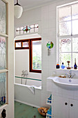 Blick durch offene Tür in weiss gefliestes Badezimmer mit Hängeleuchte und Architekturelementen in Jugendstil