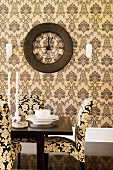 Chairs upholstered in ornamental patterned fabric at set table in front of patterned wallpaper and vintage wall clock