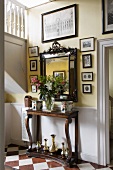 Bouquet of lilies on antique console table, mirror and old photos and drawings in entrance hall of English country house