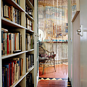 Schmaler Flur mit eingebautem Bücherregal und Blick durch offene Tür mit Fadenvorhang in der Leibung