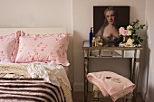 Baroque painted portrait on mirrored console table next to double bed with ruffled pillows