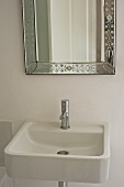 Plain ceramic sink below wall-mounted mirror with floral, etched frame