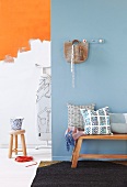 Cushions on bench in front of light blue painted wall and stool in front of wall partially painted orange