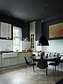Shell chairs around a black dining table below black-painted ceiling in a rustic kitchen