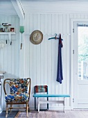 Rattan armchair with colourful cushions against white-painted wooden wall