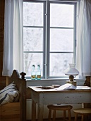 Tisch vor Fenster mit weißem Vorhang in schlichtem Schlafraum