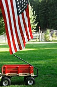 Red Wagon in a Yard with the American Flag; White Picket Fence in the Background