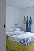 View through open door of double bed with Swedish-style bed linen in white, wood-panelled bedroom