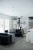 Open-plan, black and white interior with comfortable sofas and original DIY shelving around wood-burning stove