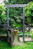 Summery garden - open garden gate with tall, wooden door-like frame and view of potted plant