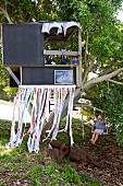 Children in modern, black tree house with ribbon curtain and boy on swing