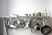 Various stainless steel pots and pans hanging from wall-mounted shelf