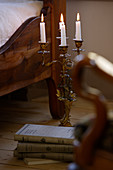 Lit candles in four-armed candlestick on floor next to bed in country-style bedroom