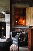 View of lit candles in niche with open wooden door above black leather armchair in rustic room with open fireplace