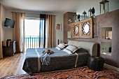 Double bed against masonry partition with wall-mounted mirrors and open balcony door with sea view
