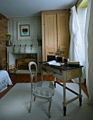 Pale colours and natural wood in bedroom with newly upholstered antique chair at antique bureau